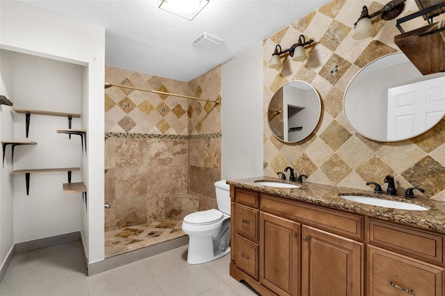 bathroom with toilet, tasteful backsplash, a tile shower, vanity, and tile patterned flooring