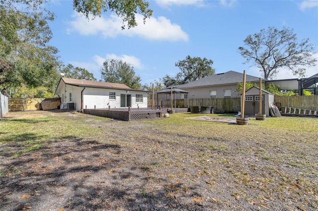 rear view of property with a lawn, a deck, a gazebo, central air condition unit, and a storage unit