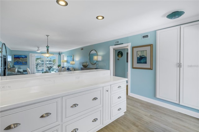 kitchen featuring white cabinetry, hanging light fixtures, crown molding, and light hardwood / wood-style flooring