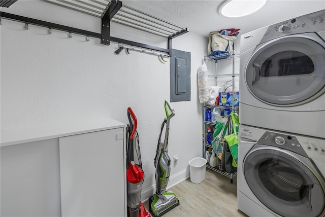 clothes washing area with stacked washer / drying machine, electric panel, a textured ceiling, and light hardwood / wood-style flooring