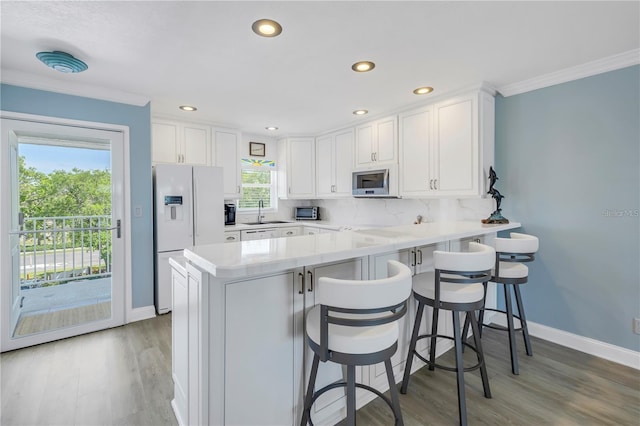 kitchen featuring white cabinetry, white fridge with ice dispenser, kitchen peninsula, and a breakfast bar