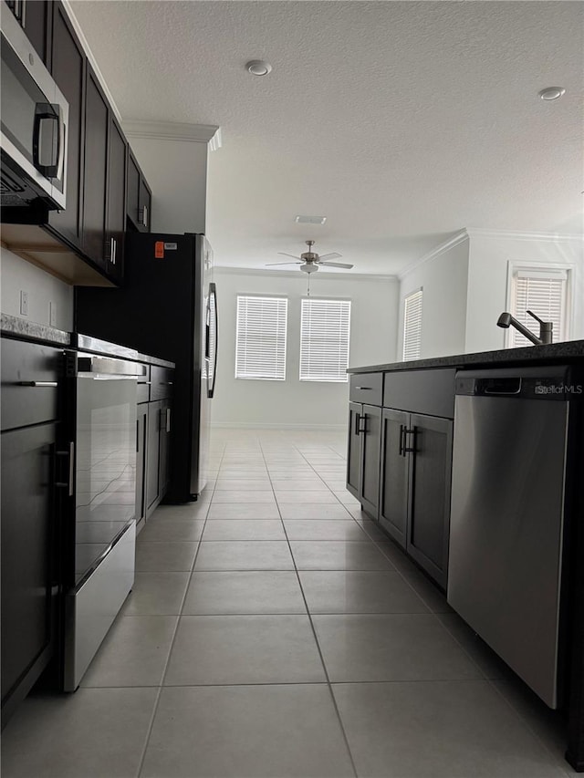 kitchen featuring light tile patterned flooring, appliances with stainless steel finishes, ornamental molding, ceiling fan, and a textured ceiling