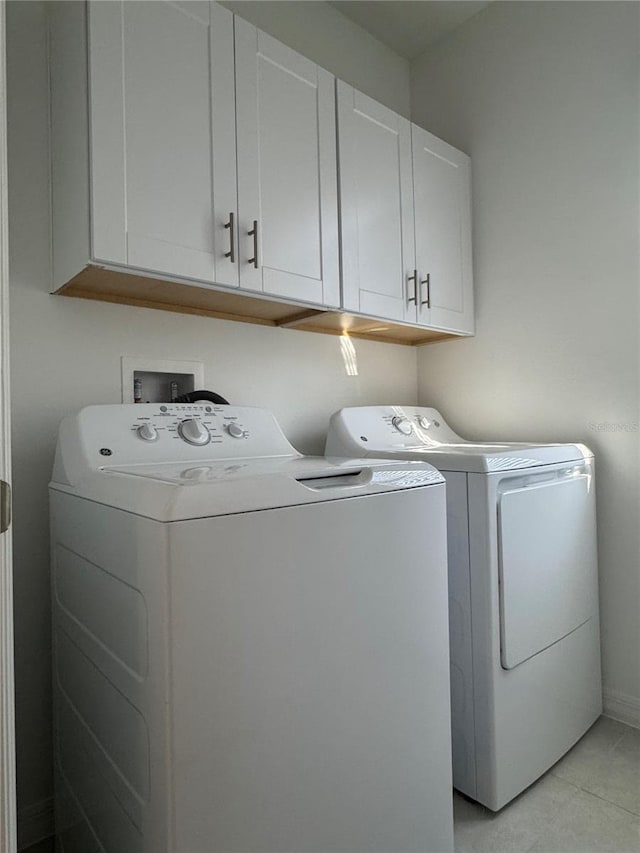 washroom with light tile patterned flooring, cabinets, and washing machine and dryer