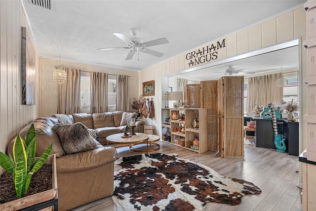 living room with light hardwood / wood-style flooring, ornamental molding, wooden walls, and ceiling fan