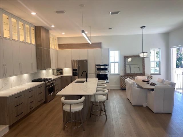 kitchen featuring high end appliances, white cabinetry, decorative light fixtures, and a center island with sink