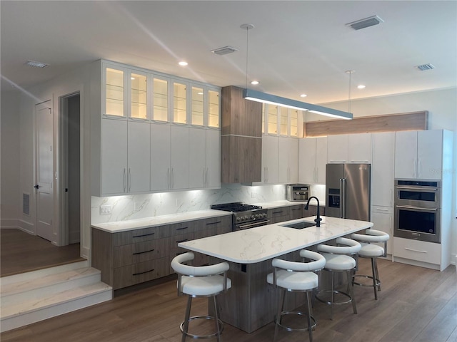 kitchen with white cabinetry, sink, backsplash, premium appliances, and a center island with sink