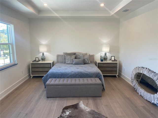 bedroom with a tray ceiling and light hardwood / wood-style flooring