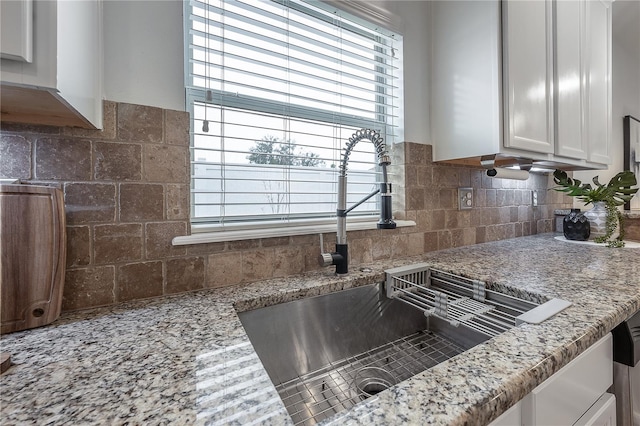 kitchen with tasteful backsplash, light stone countertops, sink, and white cabinets