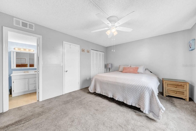 bedroom with ensuite bathroom, light colored carpet, a textured ceiling, and ceiling fan