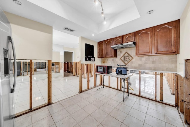 kitchen featuring stainless steel fridge, a raised ceiling, decorative backsplash, and light tile patterned floors