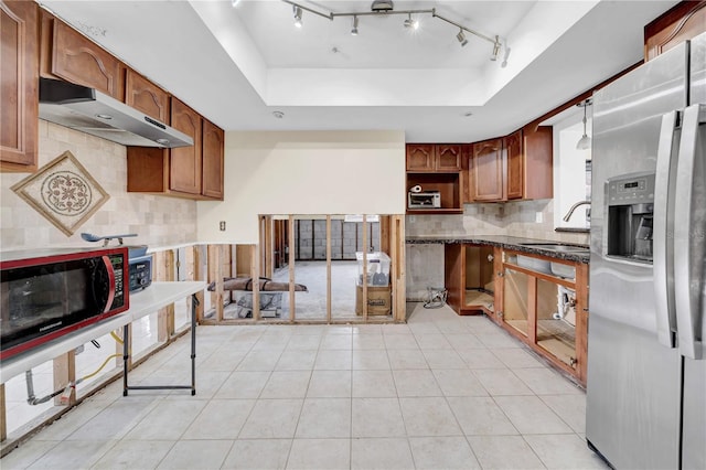 kitchen with dark stone countertops, sink, stainless steel fridge, and a raised ceiling