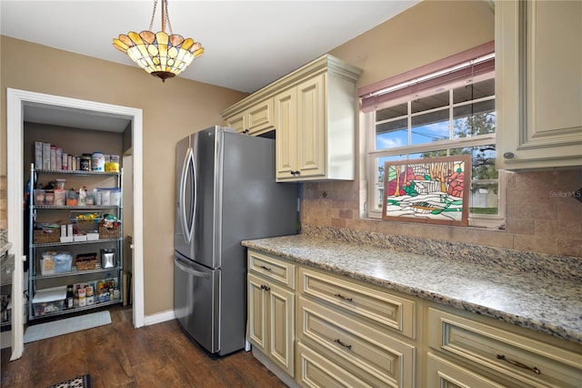 kitchen featuring decorative backsplash, stainless steel fridge, hanging light fixtures, and cream cabinetry