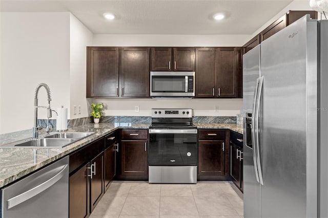 kitchen featuring appliances with stainless steel finishes, sink, light tile patterned floors, light stone counters, and dark brown cabinetry