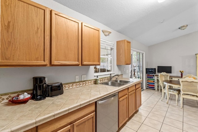 kitchen featuring light tile patterned flooring, sink, tile countertops, vaulted ceiling, and stainless steel dishwasher