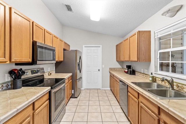 kitchen with light tile patterned flooring, lofted ceiling, sink, a textured ceiling, and appliances with stainless steel finishes