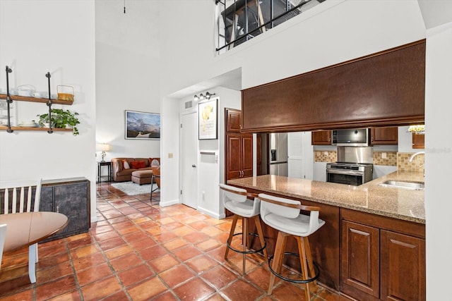 kitchen featuring stove, a towering ceiling, sink, a breakfast bar area, and stainless steel fridge