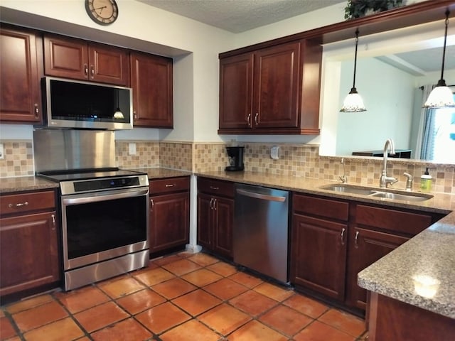 kitchen featuring appliances with stainless steel finishes, a sink, decorative backsplash, light stone counters, and decorative light fixtures