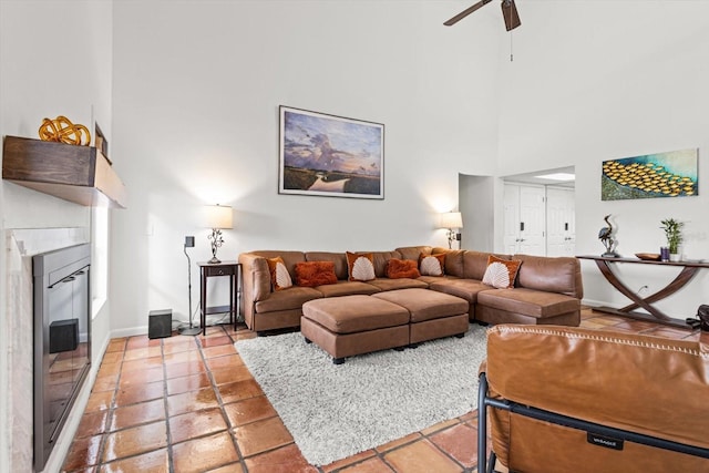living room featuring a towering ceiling, ceiling fan, baseboards, light tile patterned flooring, and a glass covered fireplace