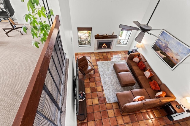 tiled living room featuring a lit fireplace, ceiling fan, and a high ceiling