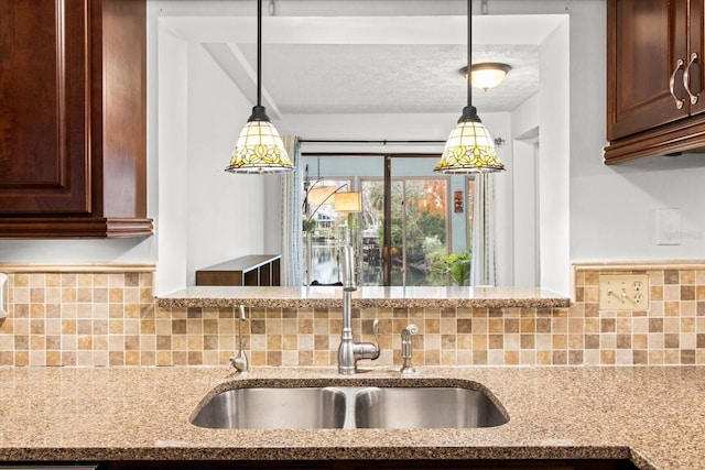 kitchen with light stone countertops, tasteful backsplash, a sink, decorative light fixtures, and a textured ceiling