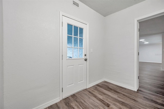 doorway to outside with dark wood-type flooring and a textured ceiling