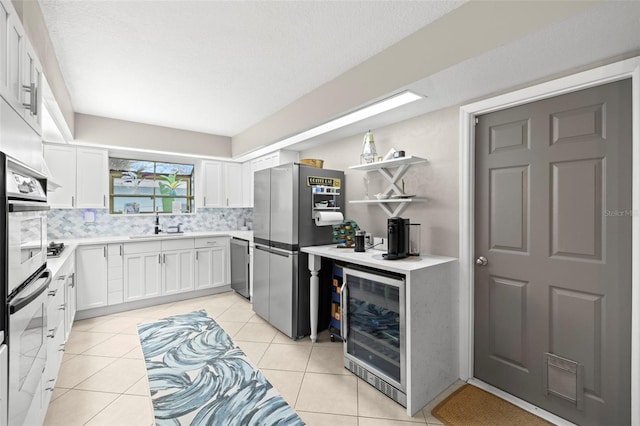 kitchen featuring wine cooler, backsplash, white cabinets, light tile patterned floors, and stainless steel appliances