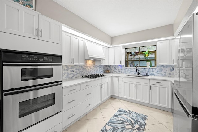 kitchen with custom exhaust hood, sink, white cabinets, tasteful backsplash, and stainless steel appliances