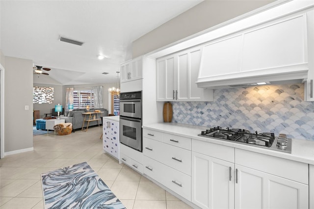 kitchen featuring ceiling fan with notable chandelier, appliances with stainless steel finishes, white cabinetry, decorative backsplash, and premium range hood