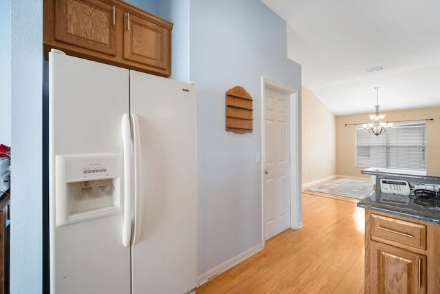 kitchen featuring a notable chandelier, dark stone countertops, light hardwood / wood-style flooring, hanging light fixtures, and white fridge with ice dispenser