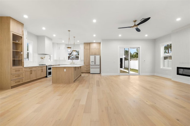 kitchen with light wood finished floors, custom range hood, white fridge with ice dispenser, a fireplace, and recessed lighting