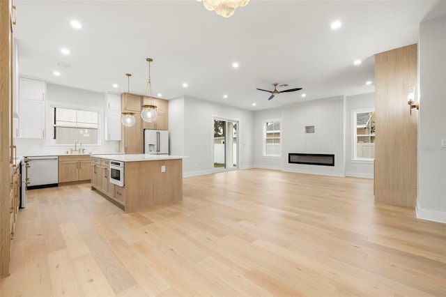 kitchen featuring white appliances, a sink, light wood-style floors, a center island, and a glass covered fireplace