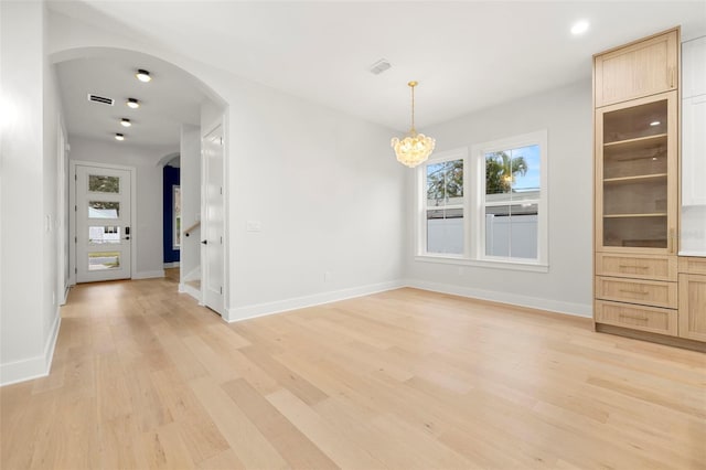 unfurnished dining area featuring arched walkways, a notable chandelier, light wood finished floors, visible vents, and baseboards