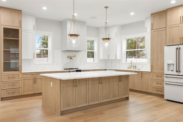 kitchen featuring white refrigerator with ice dispenser, a sink, backsplash, a center island, and light wood finished floors