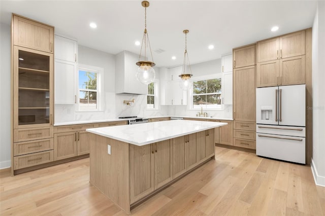 kitchen with a center island, white refrigerator with ice dispenser, a sink, light wood-type flooring, and wall chimney exhaust hood