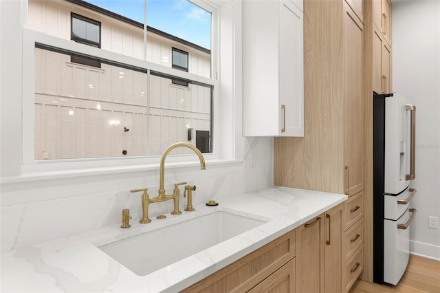 kitchen with white refrigerator with ice dispenser, a sink, light wood-style flooring, and light stone countertops