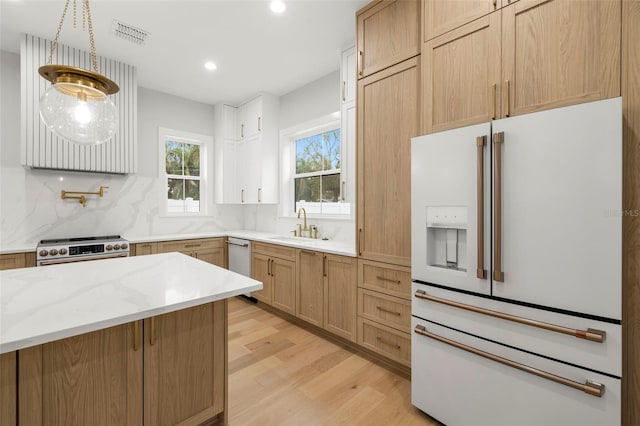 kitchen with white refrigerator with ice dispenser, stainless steel stove, decorative backsplash, a sink, and light wood-type flooring