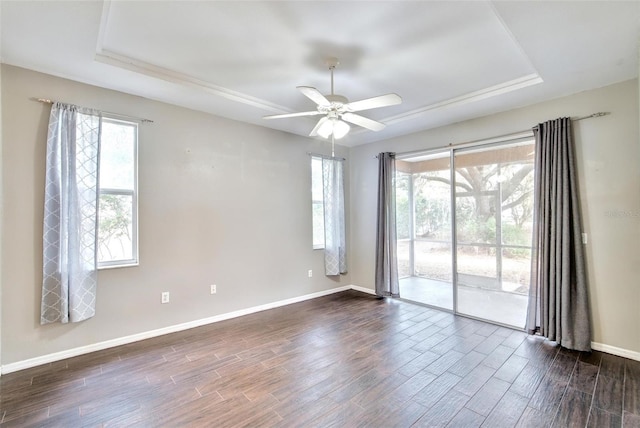 empty room featuring a raised ceiling, dark wood-type flooring, and a healthy amount of sunlight