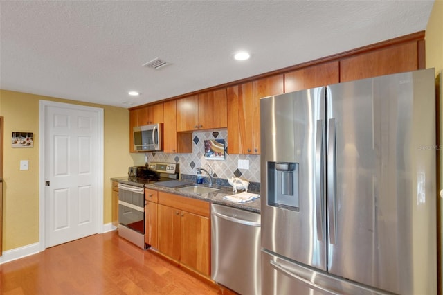 kitchen featuring sink, tasteful backsplash, light wood-type flooring, appliances with stainless steel finishes, and stone counters