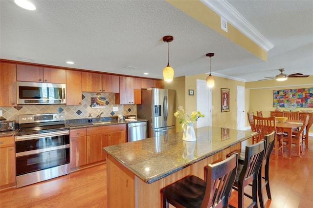 kitchen with pendant lighting, sink, backsplash, ornamental molding, and stainless steel appliances