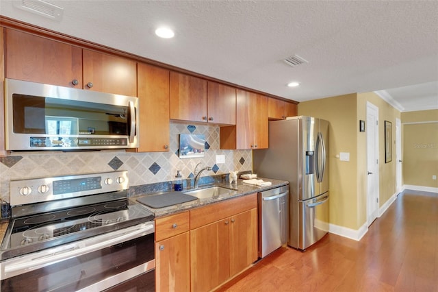 kitchen with sink, a textured ceiling, appliances with stainless steel finishes, light hardwood / wood-style floors, and decorative backsplash