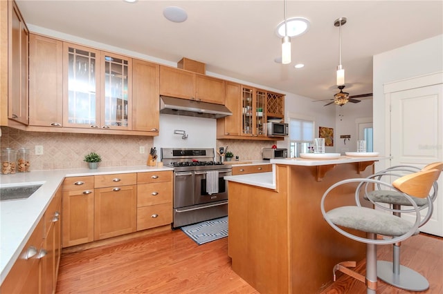 kitchen featuring stainless steel appliances, decorative light fixtures, light hardwood / wood-style floors, and a breakfast bar area