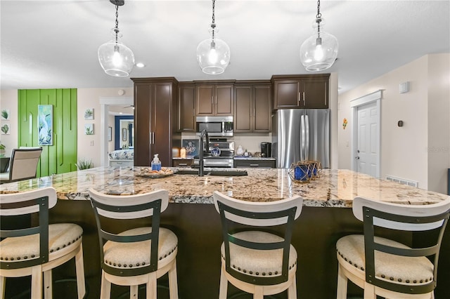 kitchen featuring pendant lighting, appliances with stainless steel finishes, sink, a breakfast bar, and dark brown cabinetry