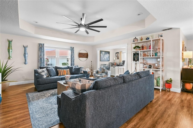 living room with ceiling fan, a raised ceiling, hardwood / wood-style floors, and a textured ceiling