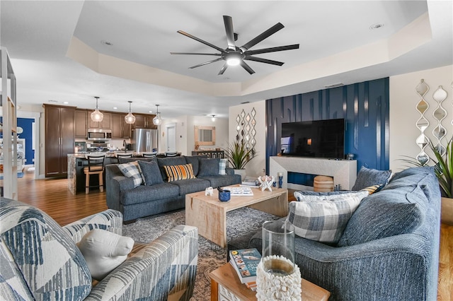 living room with ceiling fan, dark wood-type flooring, and a tray ceiling