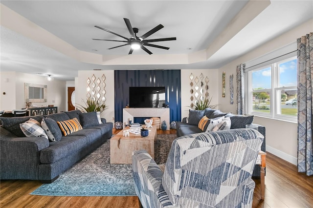 living room with wood-type flooring, ceiling fan, and a tray ceiling