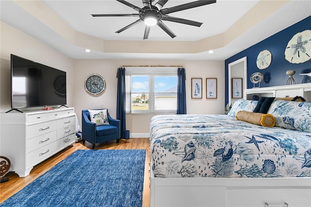 bedroom featuring ceiling fan, a raised ceiling, and light hardwood / wood-style floors