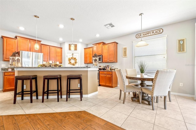 kitchen featuring light tile patterned flooring, pendant lighting, a kitchen bar, a kitchen island with sink, and stainless steel appliances