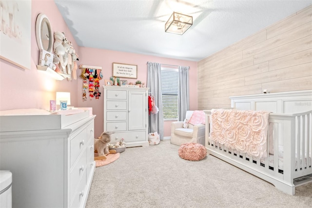 carpeted bedroom featuring a crib, wooden walls, and a textured ceiling