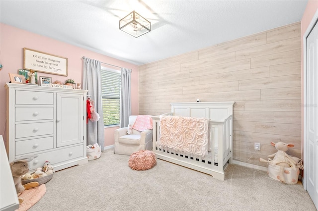 bedroom featuring light carpet, wooden walls, a nursery area, and a textured ceiling