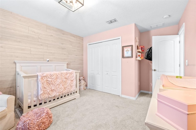 bedroom featuring wood walls, a textured ceiling, a closet, light colored carpet, and a crib